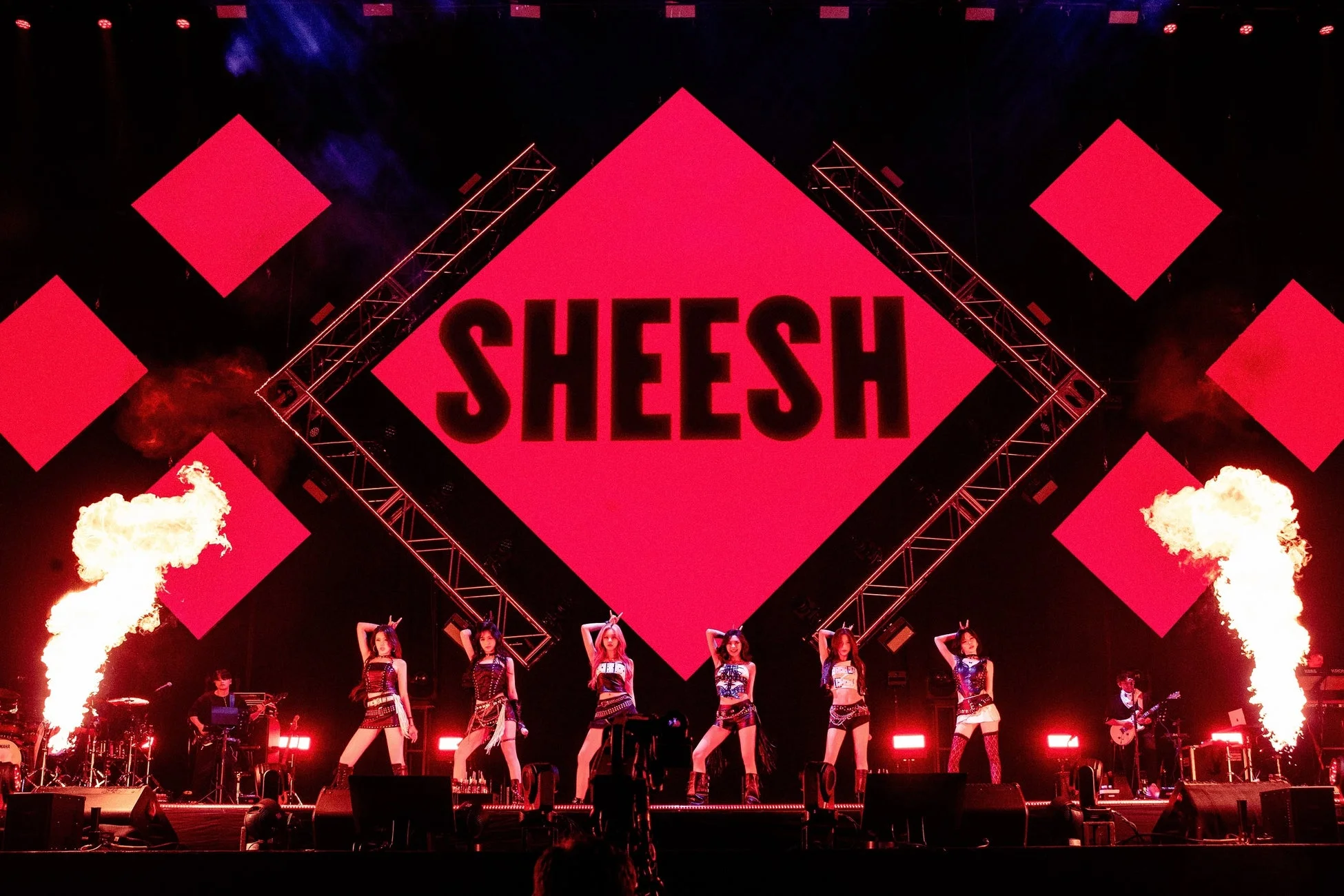 ステージ上で女性グループがパフォーマンスしている様子。背景の大きな赤いスクリーンには「SHEESH」と表示され、両サイドからは炎が吹き上がり、非常にエネルギッシュなライブの瞬間を捉えています。