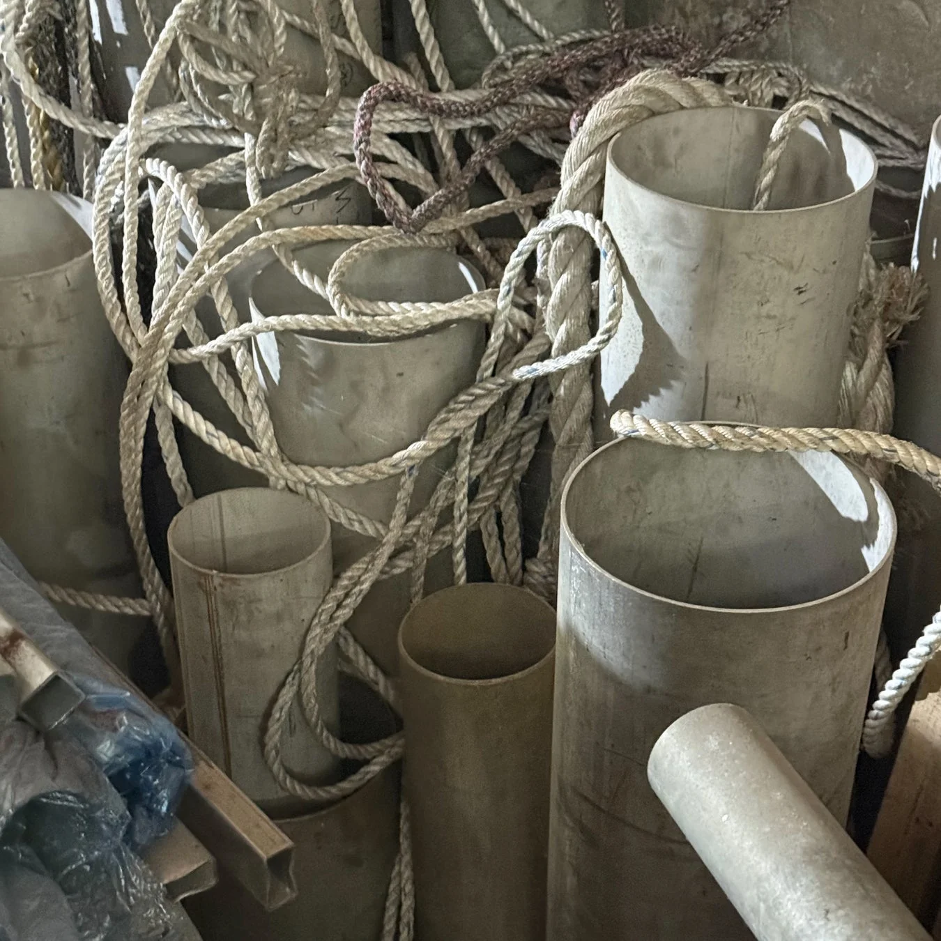 様々な太さの白いロープが、複数の金属製のパイプや筒に絡みつくように置かれている様子