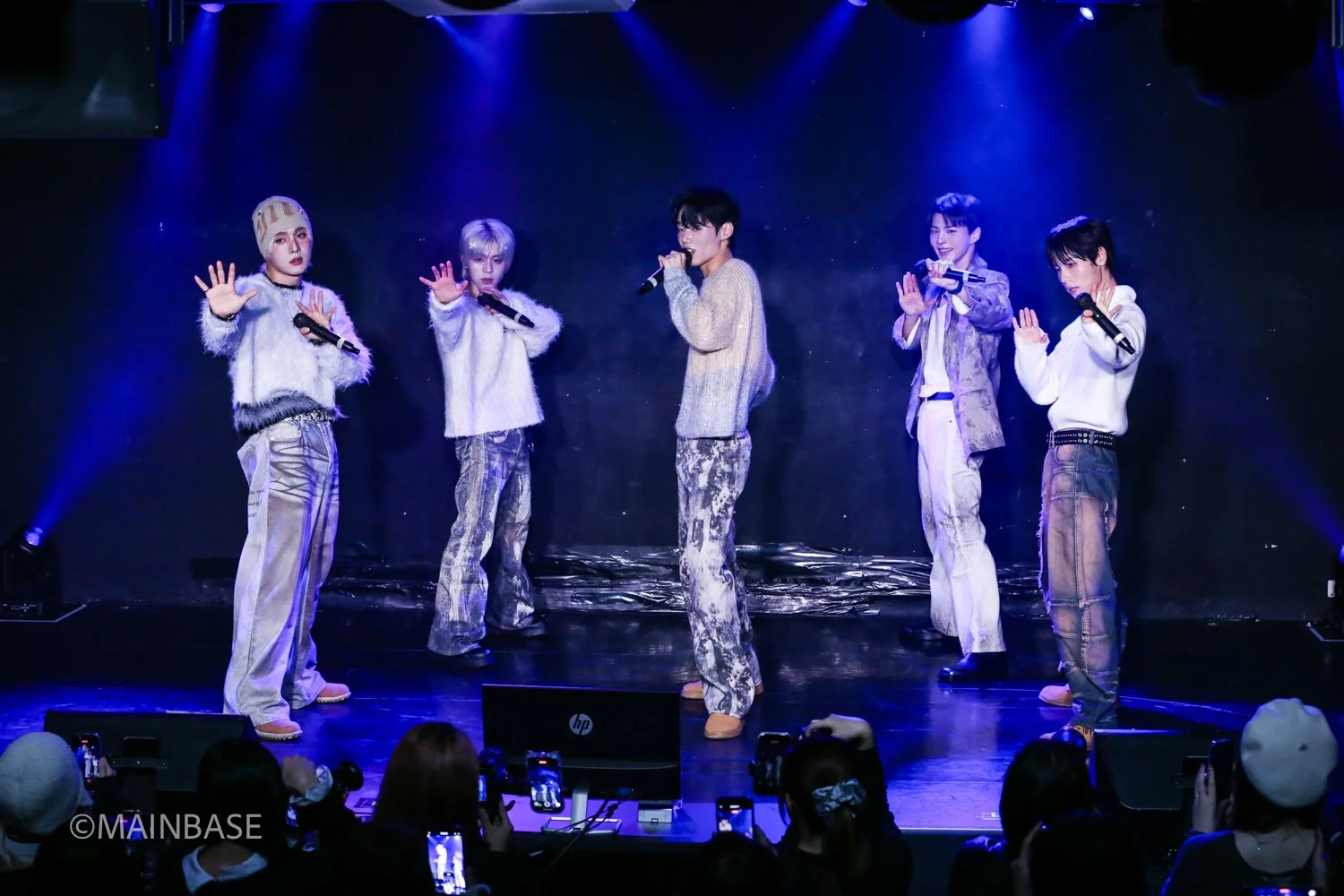 青い照明が当たるステージで、5人組の男性アイドルグループがマイクを持ちパフォーマンスを披露しています。