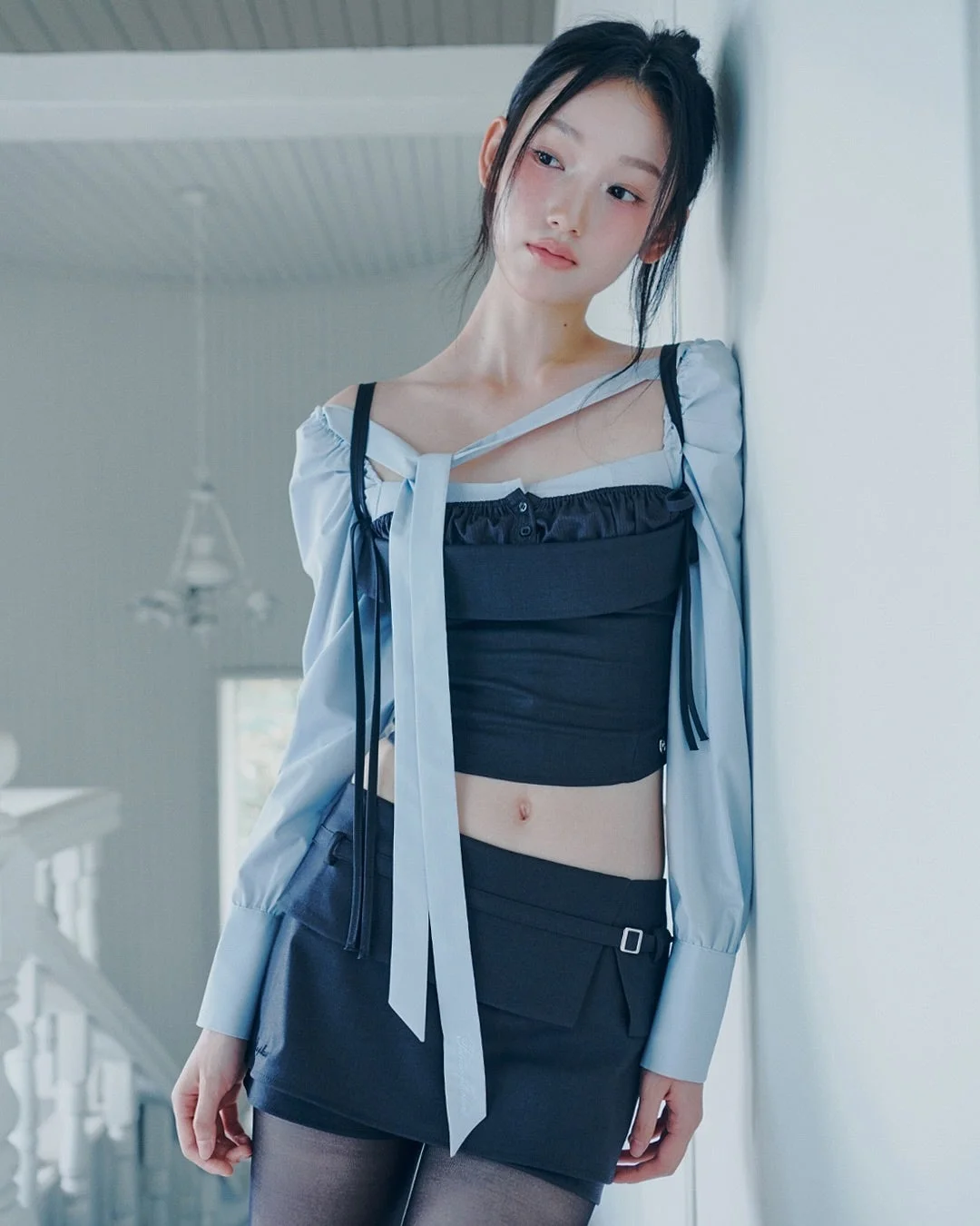 水色のブラウスと黒のクロップトップ、ミニスカートを着た女性