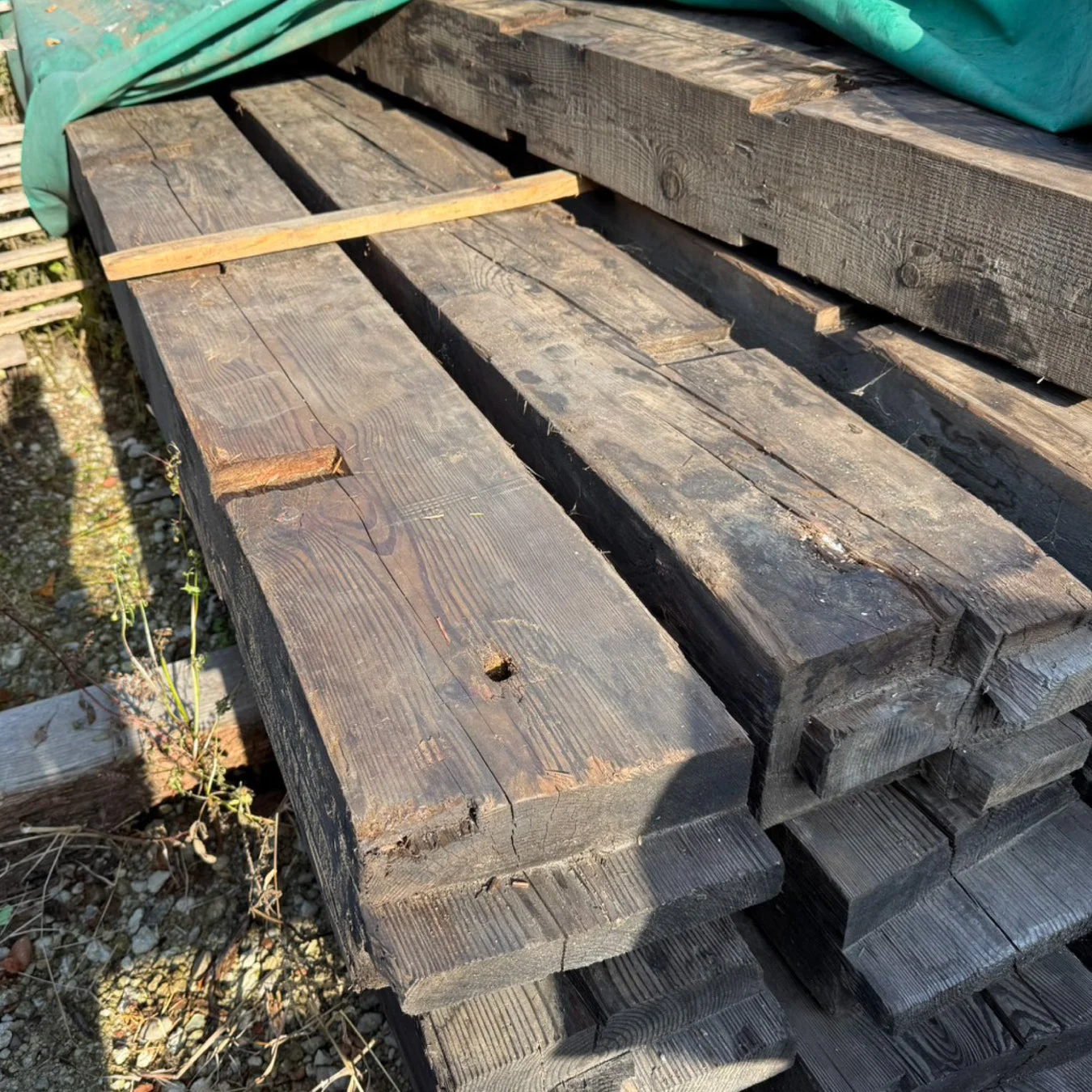 屋外に積み重ねられた、古くて風化した木材の梁の山