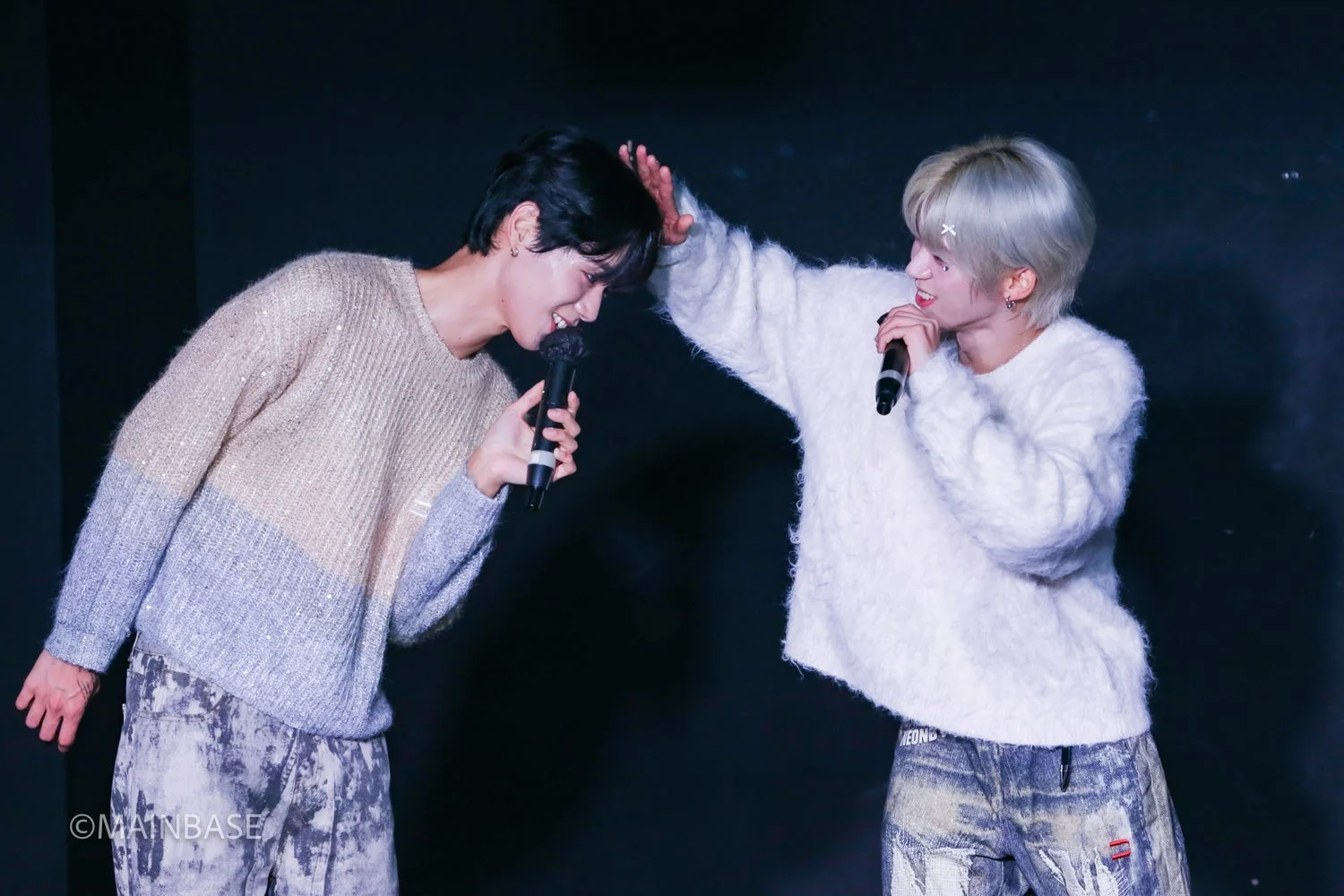 ステージ上でマイクを手に歌う二人の男性アイドルの写真。互いに顔を寄せ合い、笑顔で親密な雰囲気を醸し出している。