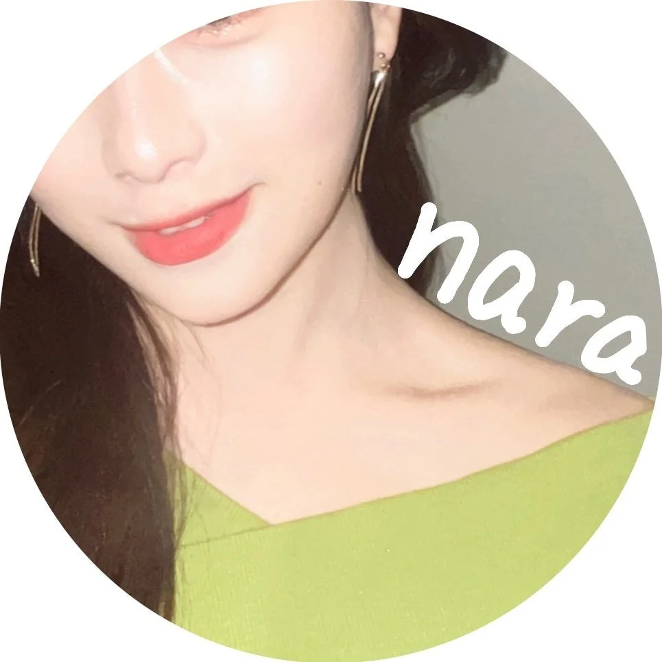 緑色の服を着た女性の顔の下半分と首元が写ったクローズアップ画像。赤いリップと長いピアスが特徴で、肩には「nara」という文字が書かれている