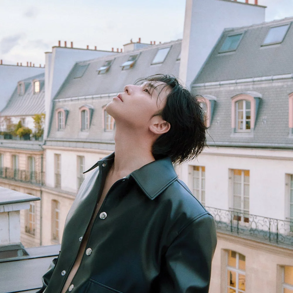 パリの街並みを背景に屋上で空を見上げるパク・ソジュンさんのショット