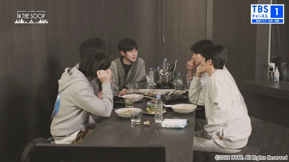 5人の若い男性がテーブルを囲んで食事をしている様子です。テーブルの中央には鍋があり、周りには料理や飲み物が並べられています。皆で談笑しており、リラックスした雰囲気で食事を楽しんでいるようです。テレビ番組「IN THE SOOP」の一場面と見られます。